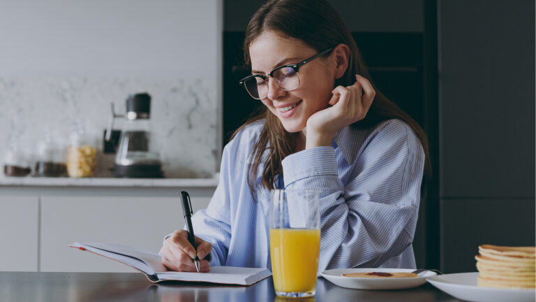 Woman writing in journal while eating breakfast