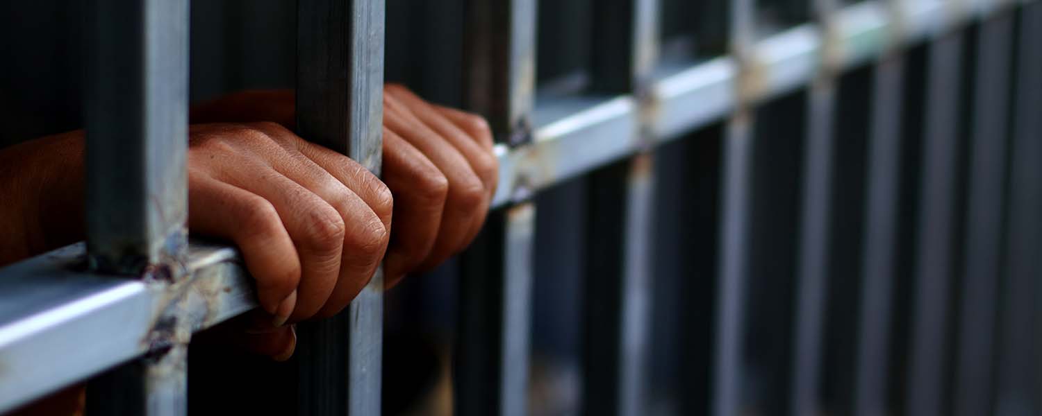 Imprisoned person's hands gripping the door of a jail cell