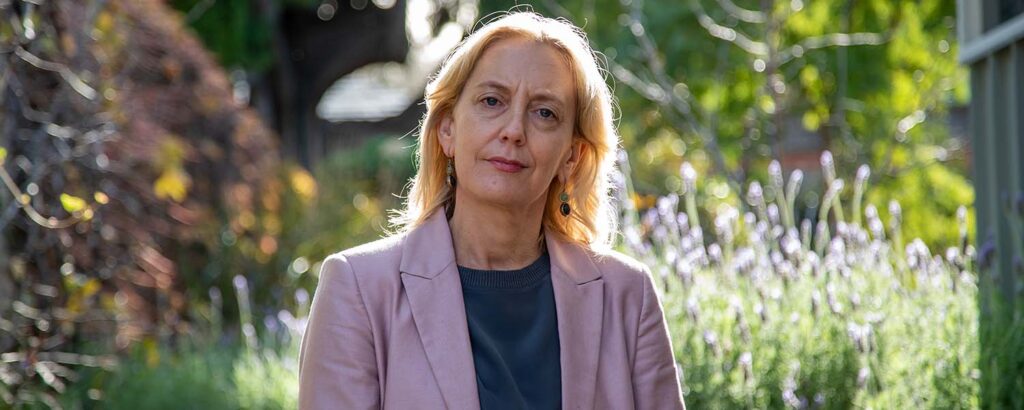 Middle-aged woman standing in her backyard with a serious expression on her face