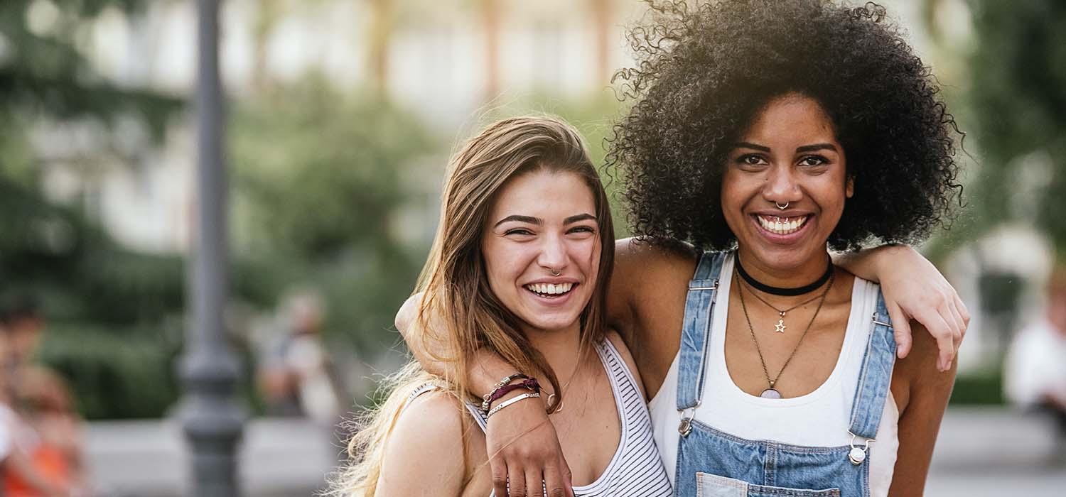 Two happy young women standing outside with arms around each other