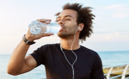 Man outside, wearing headphones and drinking water